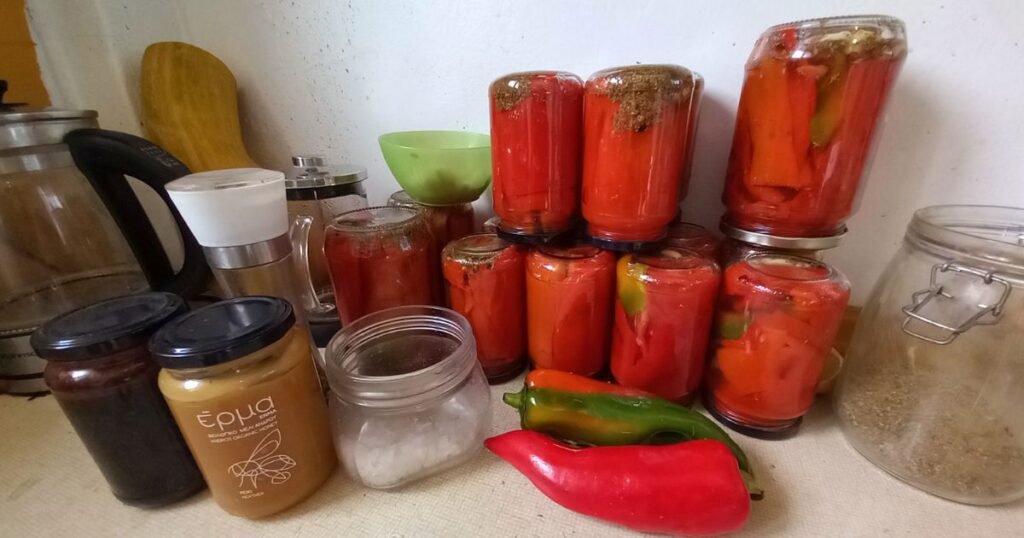 Βάζα με κόκκινη πιπεριά τουρσί, λαχανικά και χειροποίητα προϊόντα της Livada Farm πάνω σε πάγκο κουζίνας